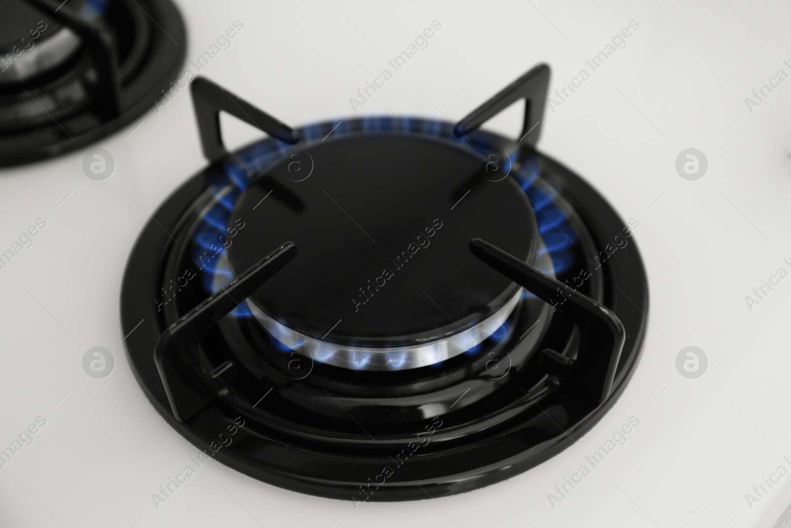 Photo of Gas burner of modern stove with burning blue flame, closeup