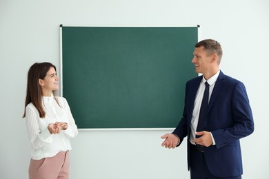 Photo of Man and woman talking near green chalkboard in classroom