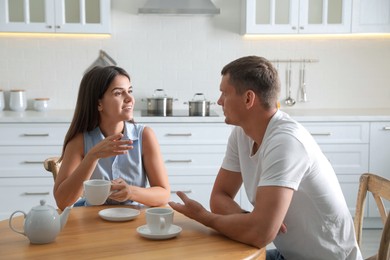 Photo of Man and woman talking while drinking tea at table in kitchen