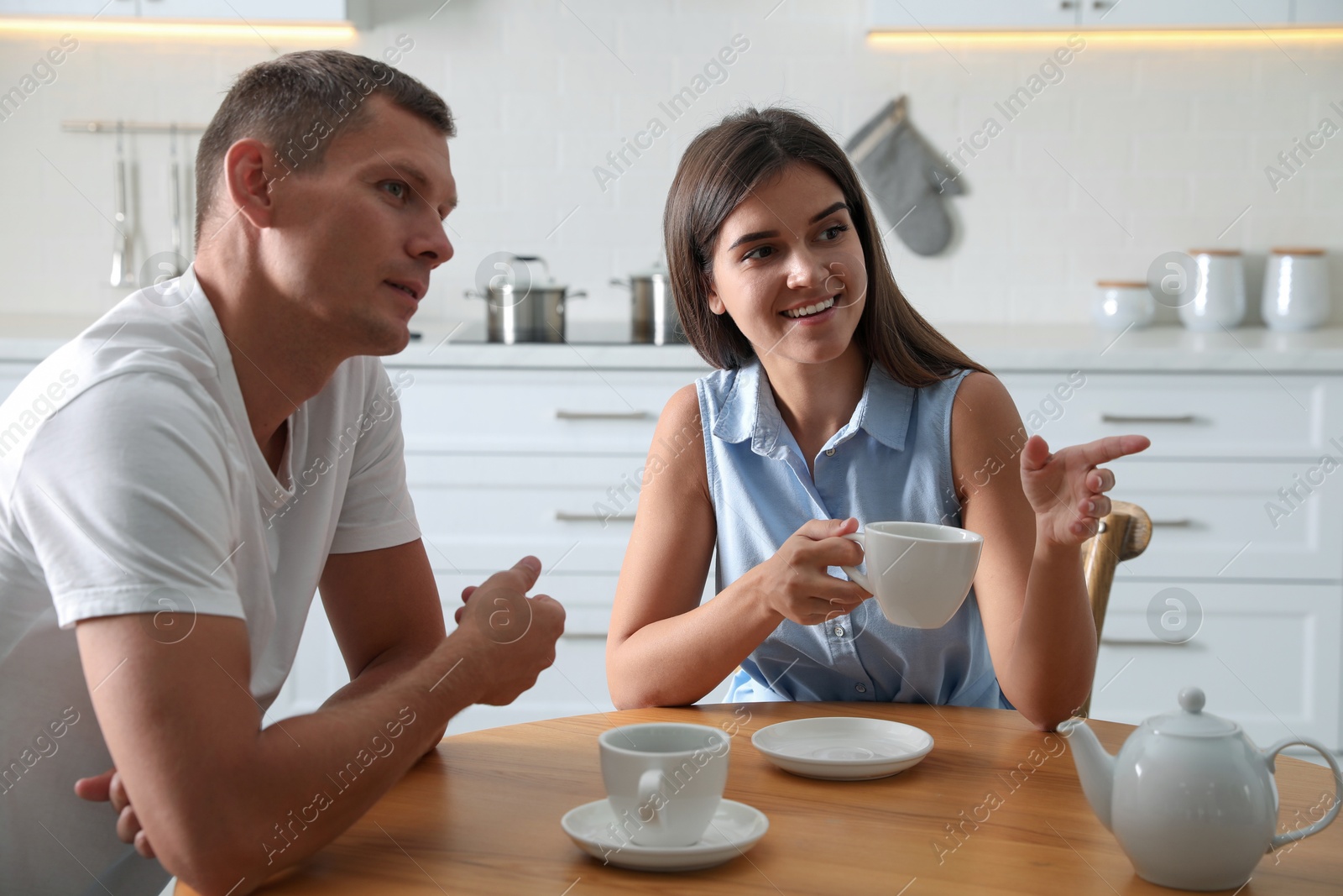 Photo of Man and woman talking while drinking tea at table in kitchen