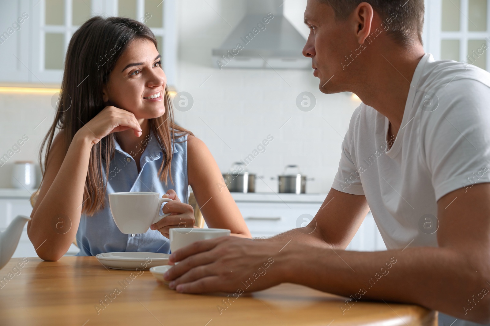 Photo of Man and woman talking while drinking tea at table in kitchen