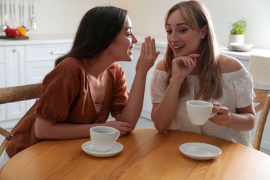 Young women talking while drinking tea at table in kitchen