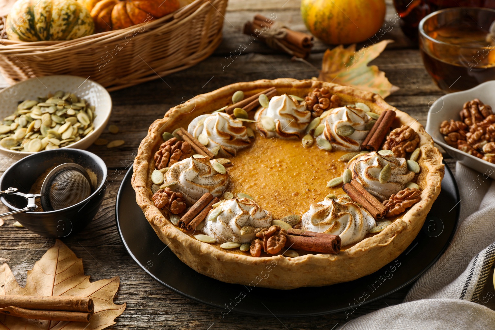 Photo of Homemade pumpkin pie with whipped cream, seeds and cinnamon on wooden table