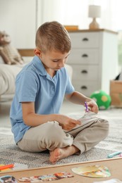 Photo of Creating vision board. Little boy cutting out picture on floor at home