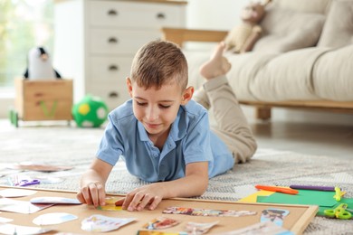 Photo of Little boy creating vision board with different pictures and other elements on floor at home