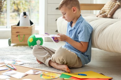 Photo of Creating vision board. Little boy cutting out picture on floor at home