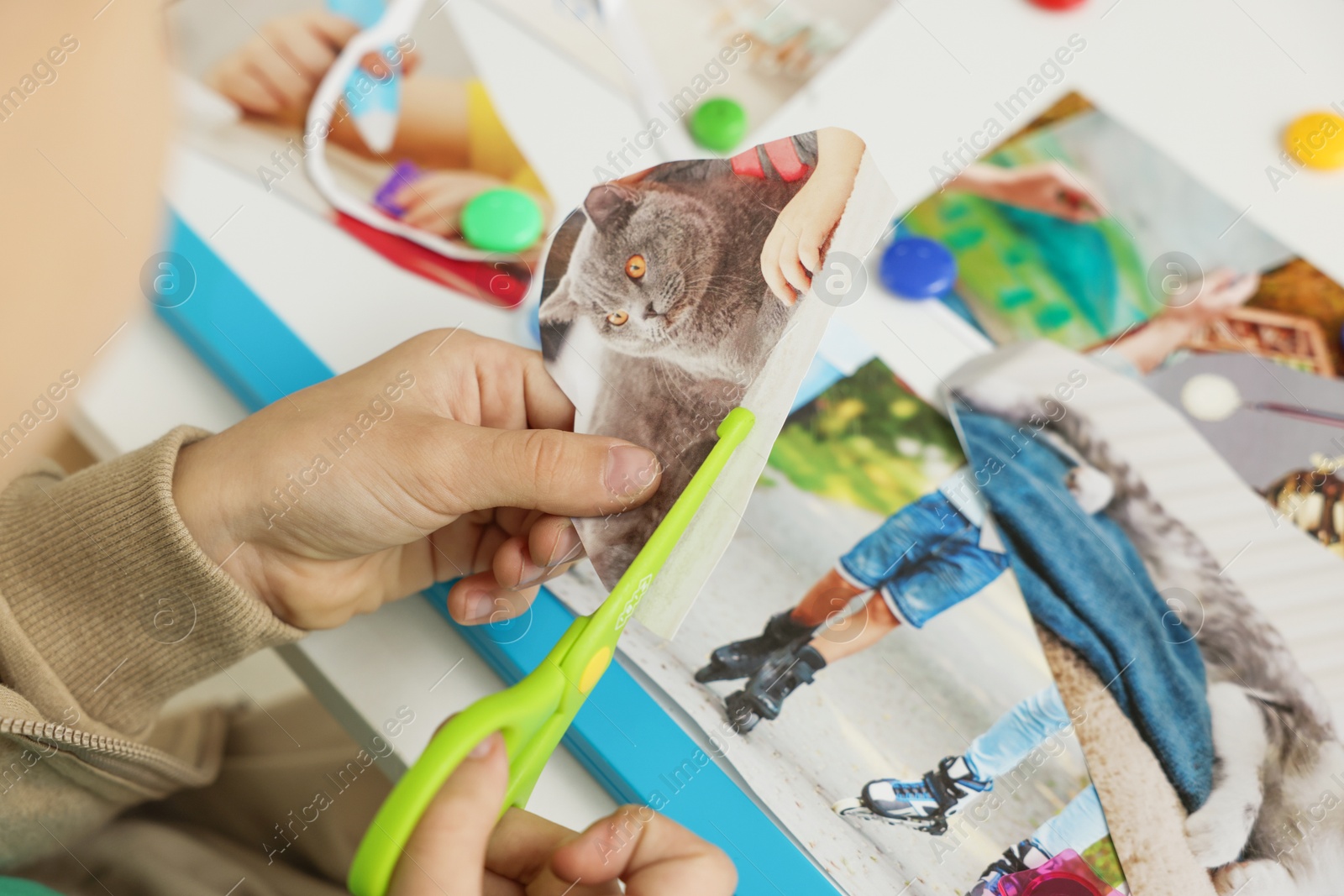 Photo of Creating vision board. Little boy cutting out picture at table indoors, closeup