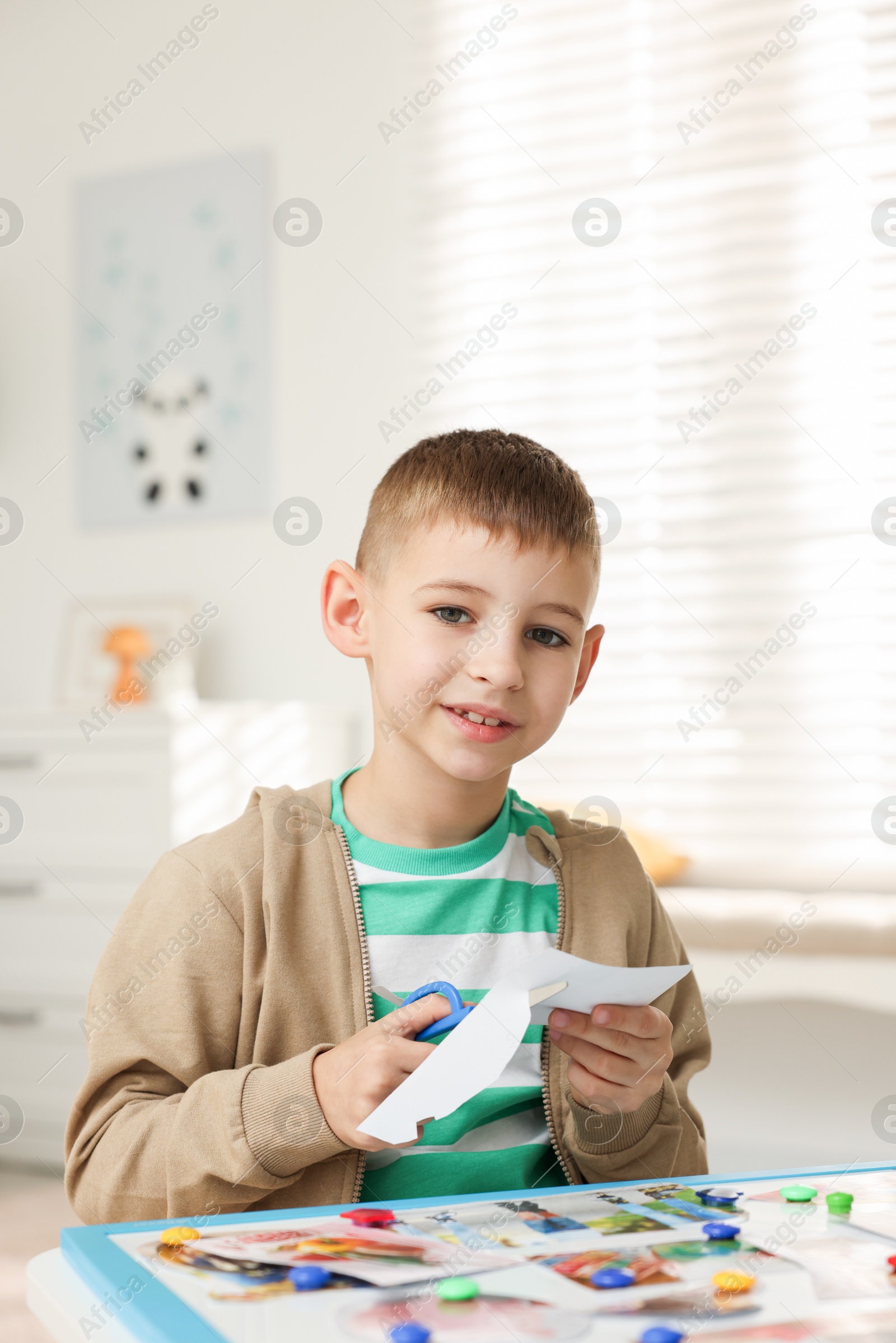 Photo of Creating vision board. Little boy cutting out picture at table indoors