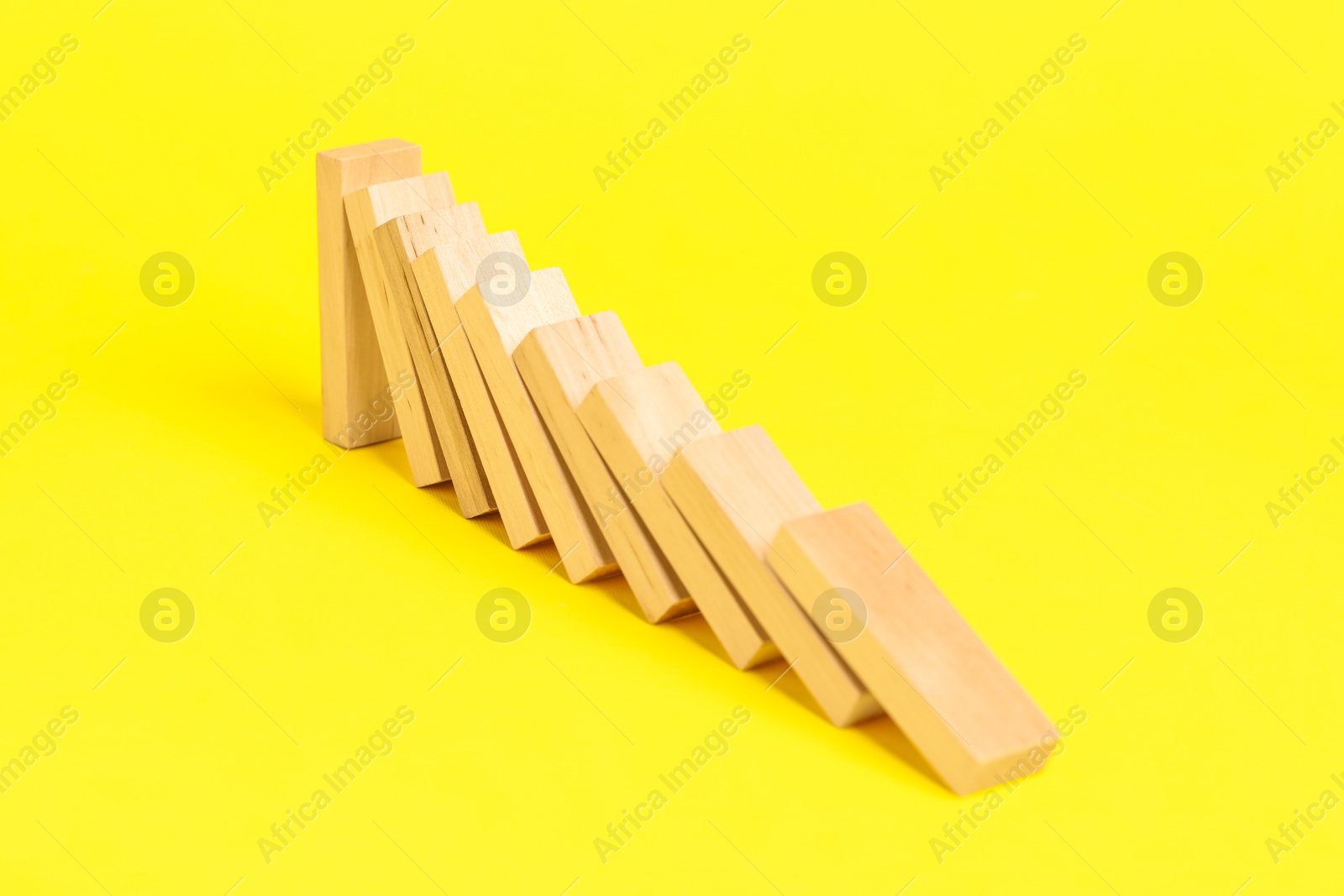 Photo of Domino effect. Wooden blocks falling on yellow background, closeup