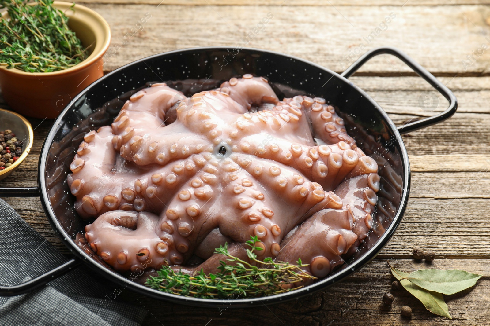 Photo of Fresh raw octopus and thyme in frying pan on wooden table, closeup