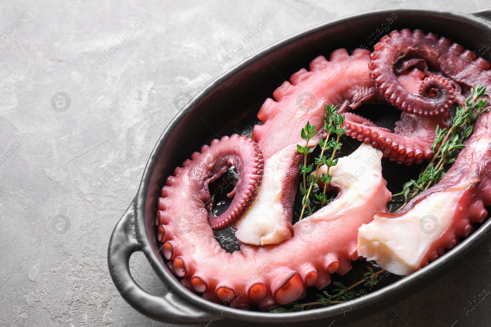 Photo of Fresh raw octopus and thyme in baking dish on grey table, closeup