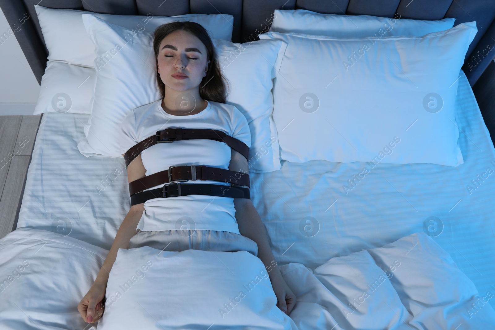 Photo of Sleepwalker fastened with belts lying in bed, top view