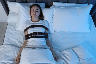 Sleepwalker fastened with belts lying in bed, top view