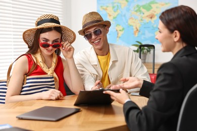 Photo of Happy couple planning vacation with travel agent at wooden table in office