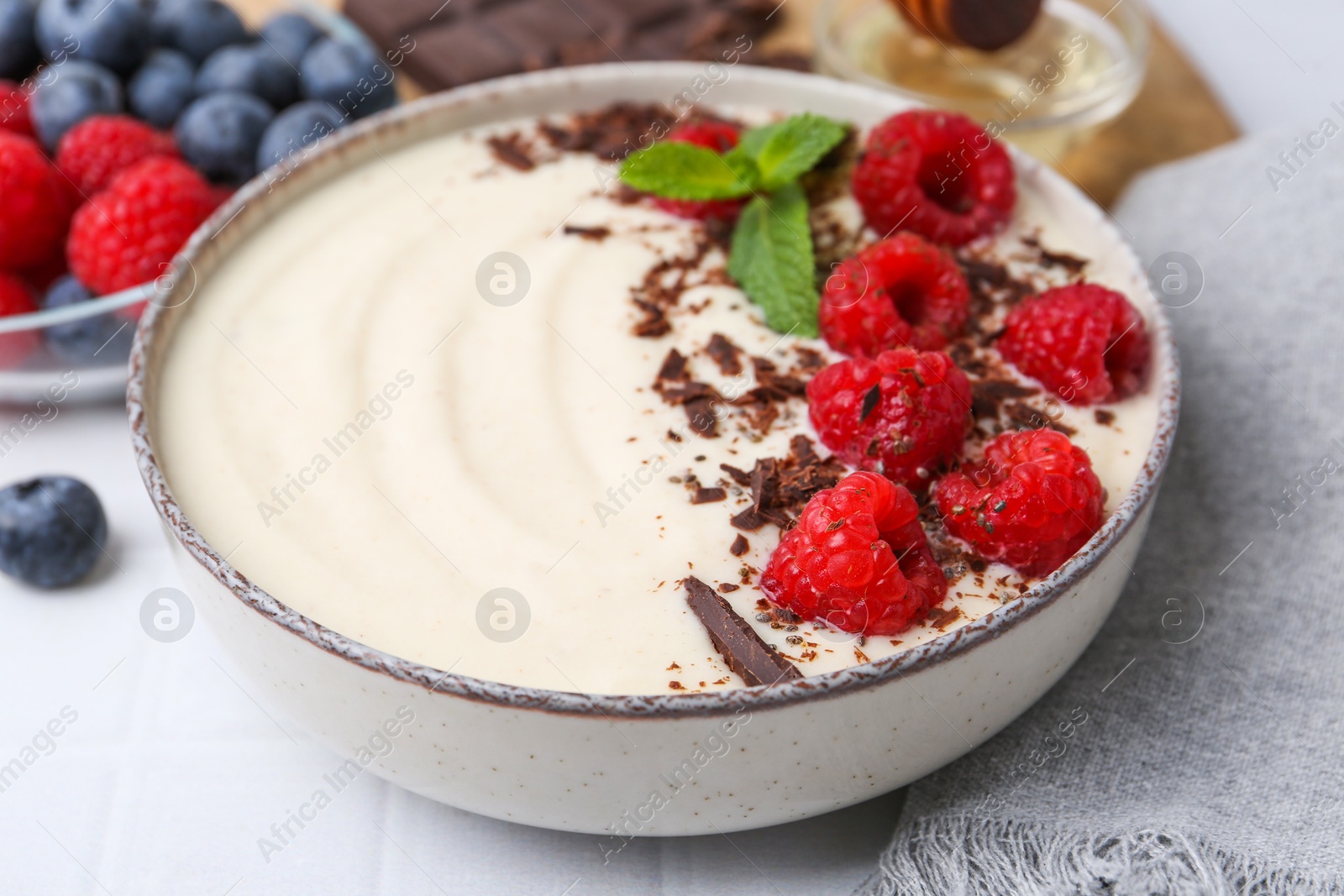 Photo of Tasty cooked semolina porridge with raspberries, chocolate and mint on white table, closeup