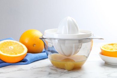 Photo of Plastic juicer and fresh oranges on white marble table, closeup