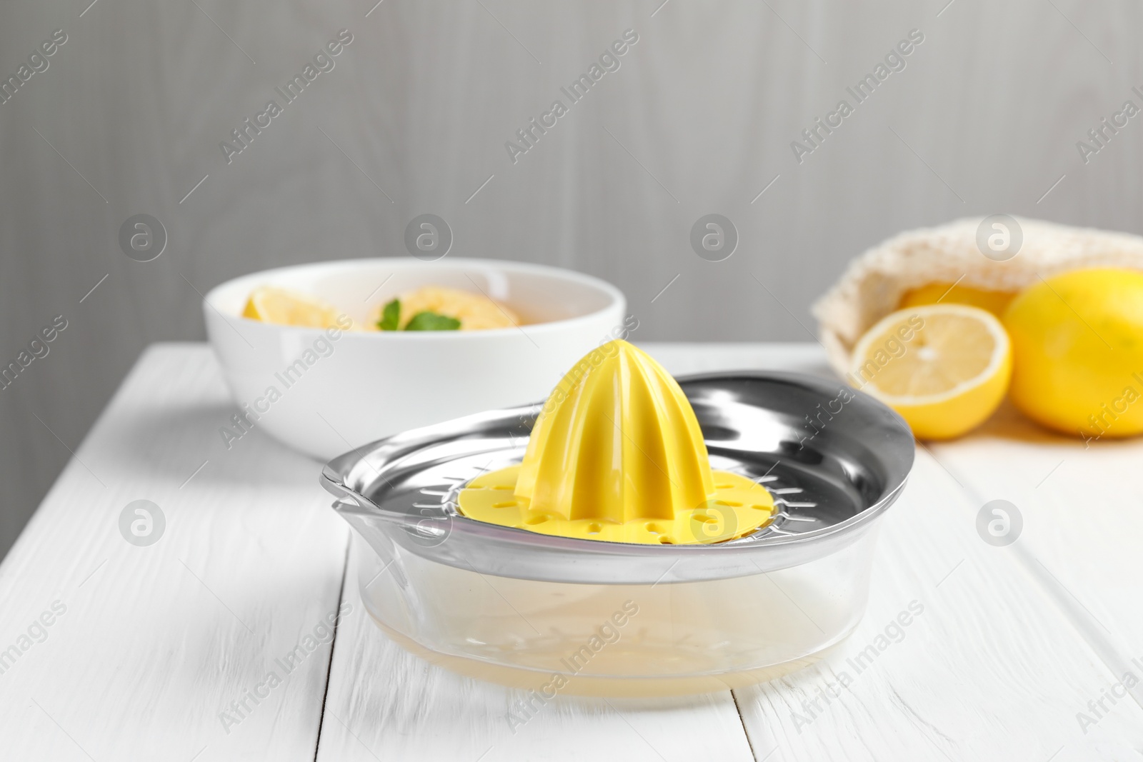 Photo of Plastic juicer and fresh lemons on white wooden table, closeup