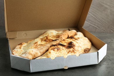 Photo of Delicious calzones in cardboard box on grey textured table, closeup