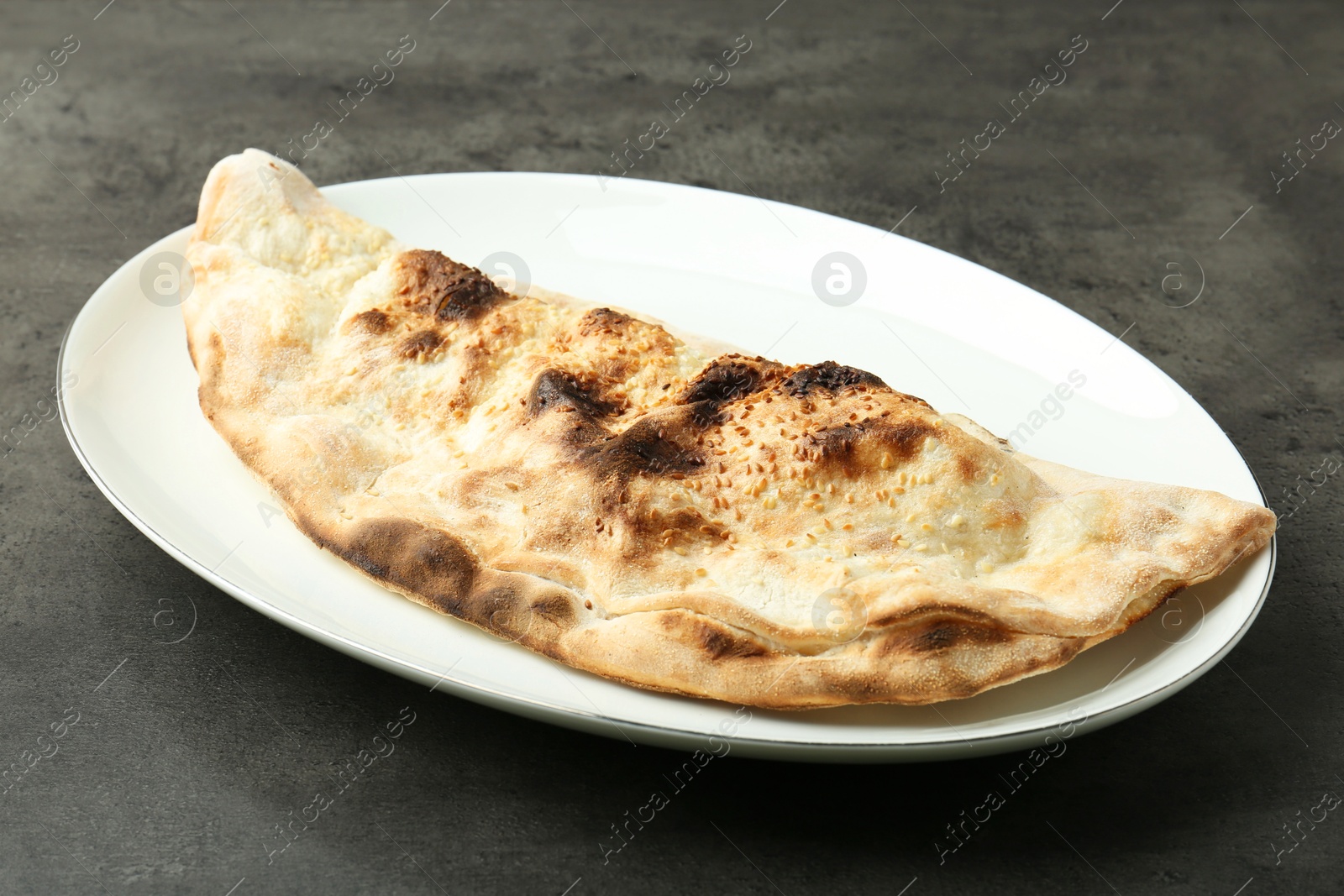 Photo of One delicious calzone on grey textured table, closeup