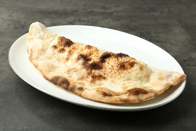 Photo of One delicious calzone on grey textured table, closeup