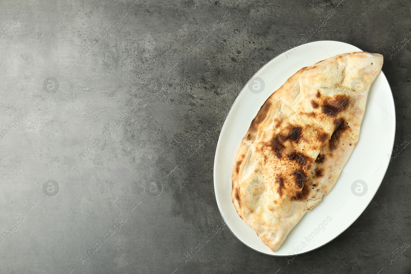 Photo of One delicious calzone on grey textured table, top view. Space for text