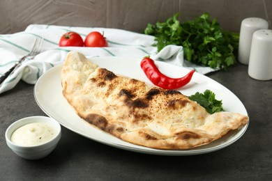 Photo of Delicious calzone served with sauce on grey table