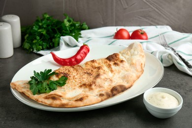 Photo of Delicious calzone served with sauce on grey table