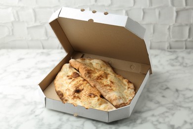 Photo of Delicious calzones in cardboard box on white marble table