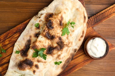 Photo of Board with tasty calzone, parsley and sauce on wooden table, top view