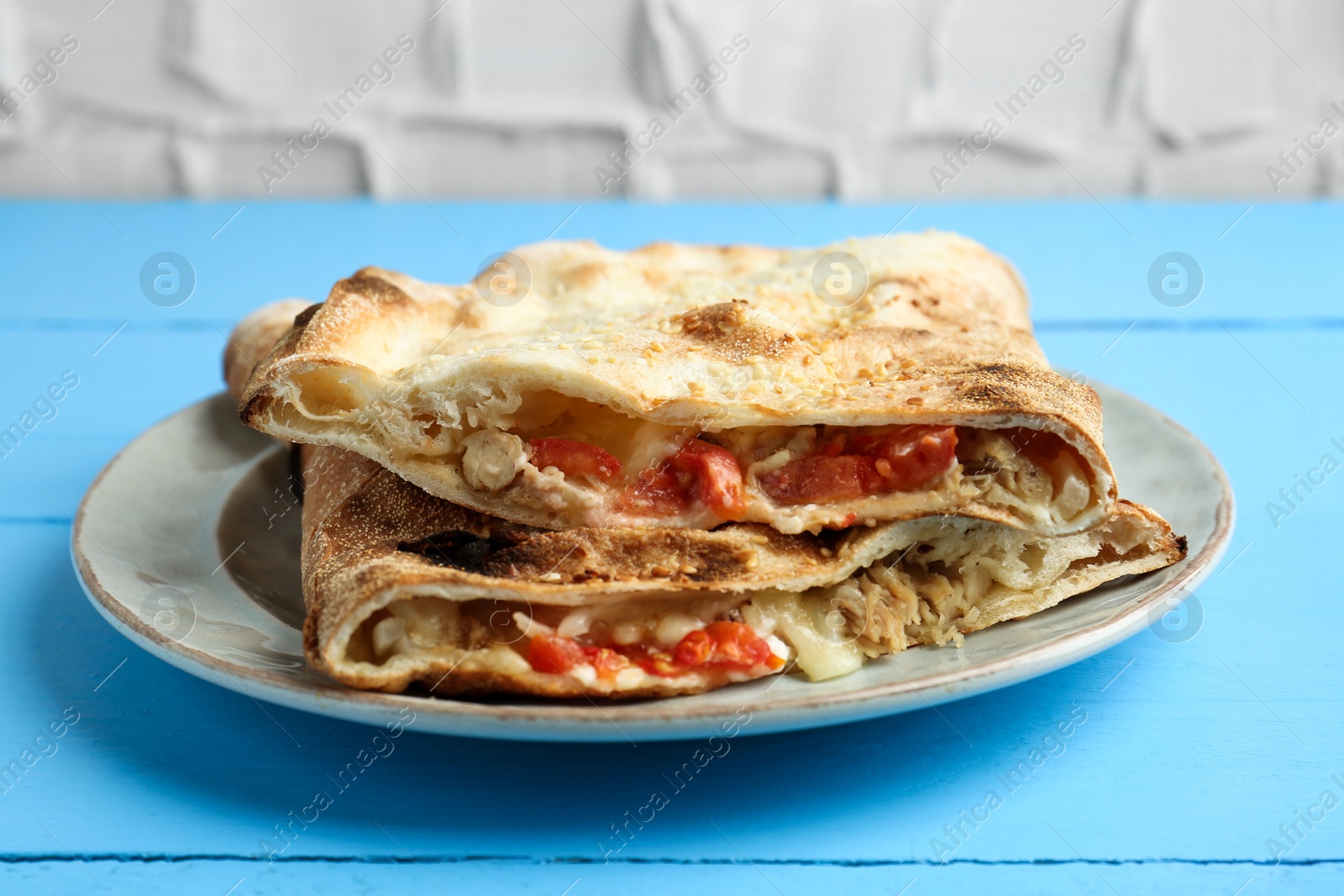 Photo of Halves of tasty calzone with meat, cheese and tomato on light blue wooden table, closeup