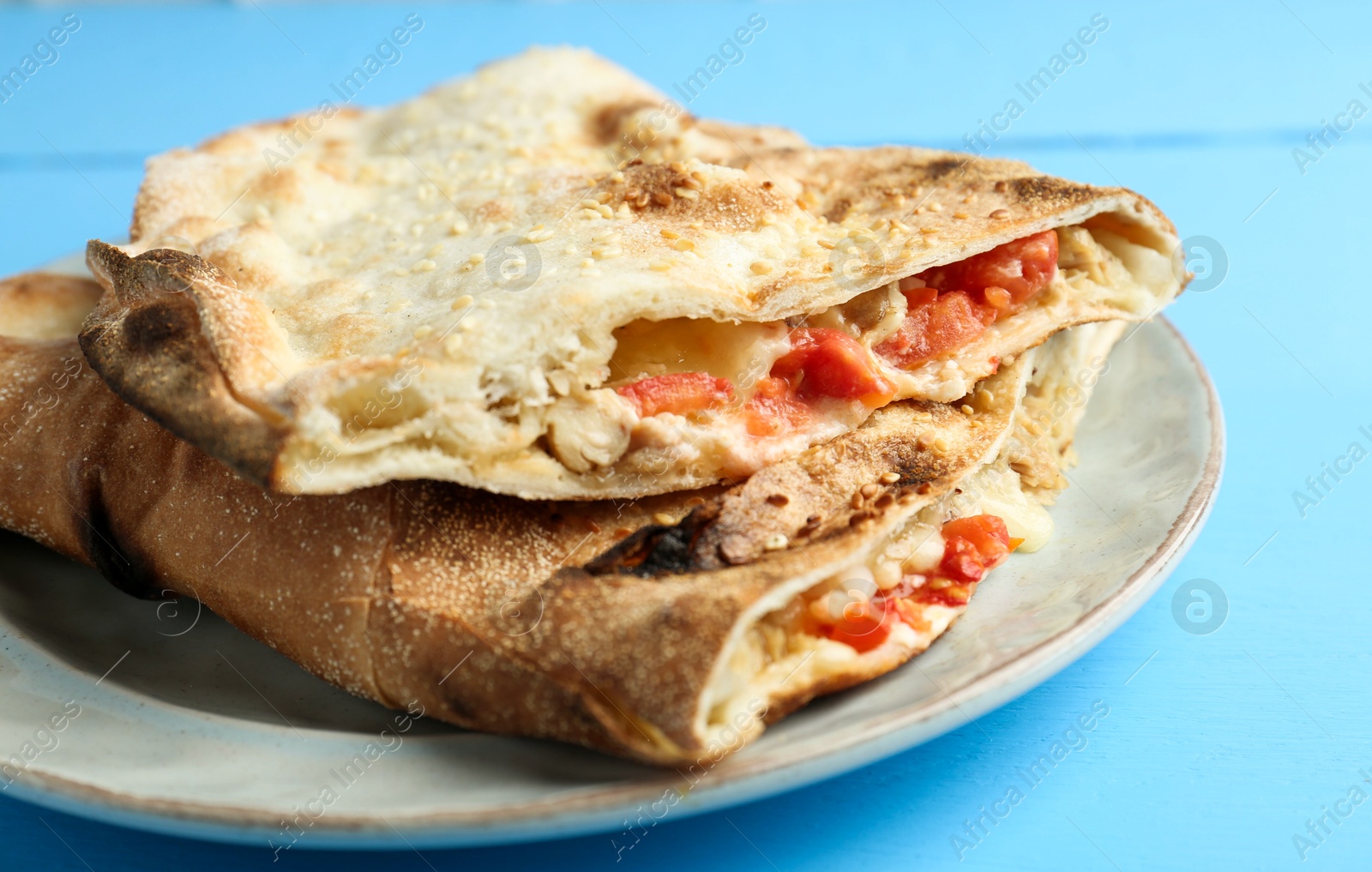 Photo of Halves of tasty calzone with meat, cheese and tomato on light blue wooden table, closeup