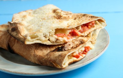 Photo of Halves of tasty calzone with meat, cheese and tomato on light blue wooden table, closeup