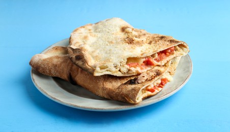 Photo of Halves of tasty calzone with meat, cheese and tomato on light blue wooden table, closeup