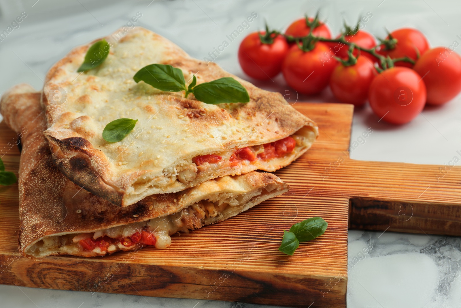 Photo of Halves of tasty calzone with meat, cheese, basil and tomato on white marble table, closeup