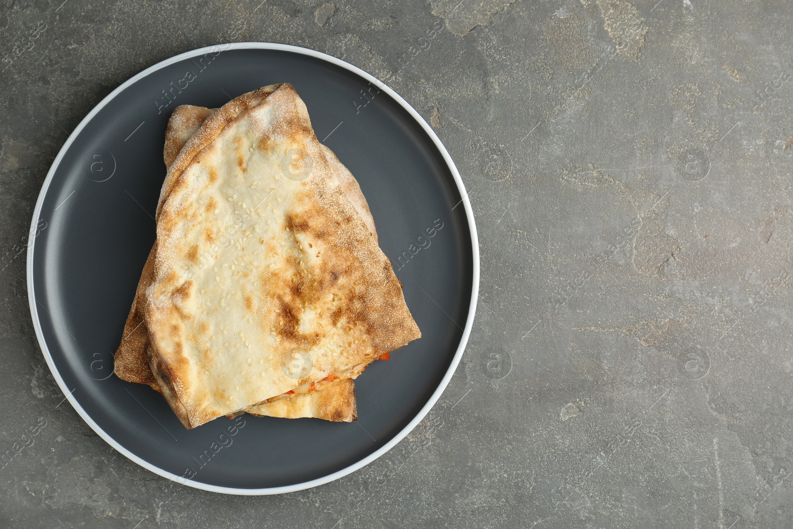 Photo of Halves of tasty calzone on grey textured table, top view. Space for text