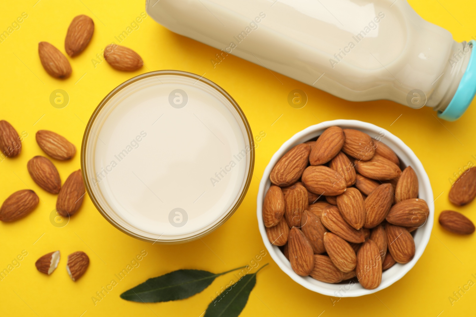 Photo of Fresh nut milk, almonds and green leaves on yellow background, flat lay