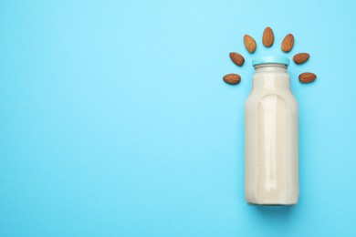 Fresh nut milk in glass bottle and almonds on light blue background, top view. Space for text