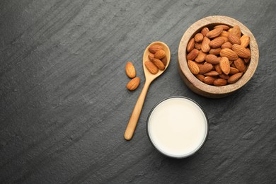 Fresh almond milk in glass, spoon and nuts on black table, top view. Space for text