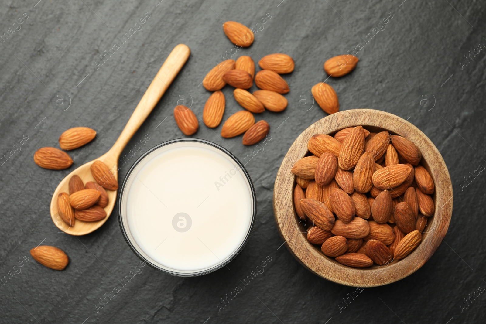 Photo of Fresh almond milk in glass, spoon and nuts on black table, top view