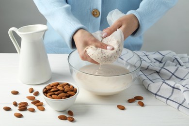 Woman making almond milk at white wooden table, closeup