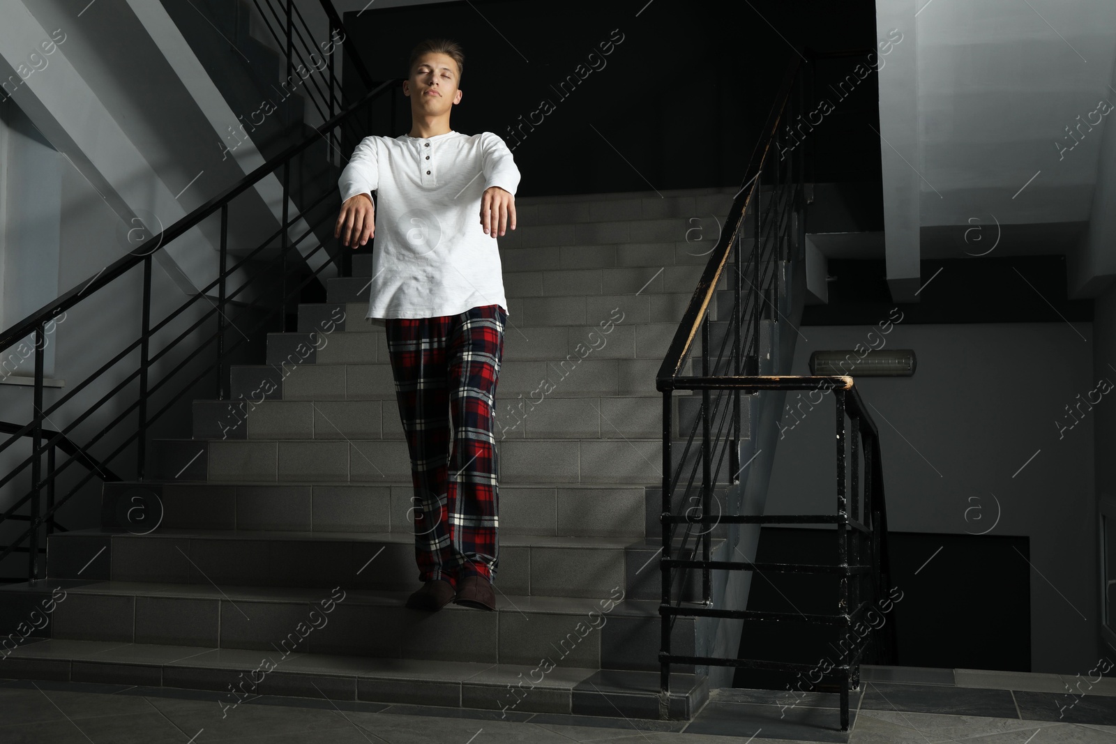 Photo of Young man suffering from sleepwalking on stairs indoors