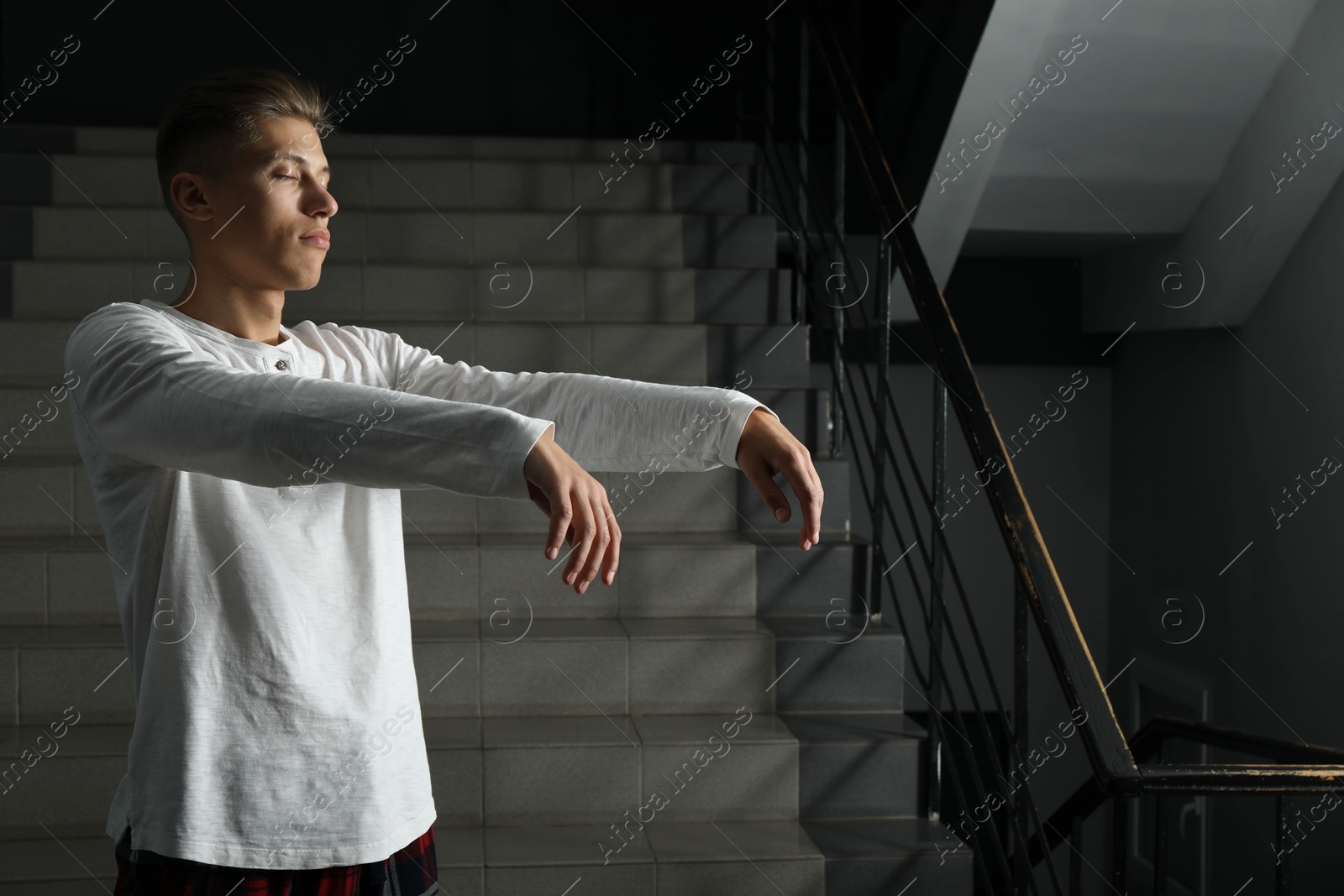 Photo of Young man suffering from sleepwalking on stairs indoors, space for text