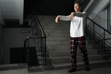 Photo of Young man suffering from sleepwalking on stairs indoors, space for text