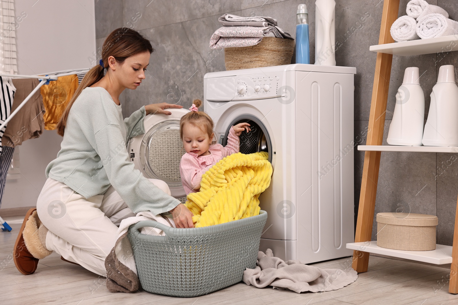 Photo of Housewife with her little daughter doing laundry at home