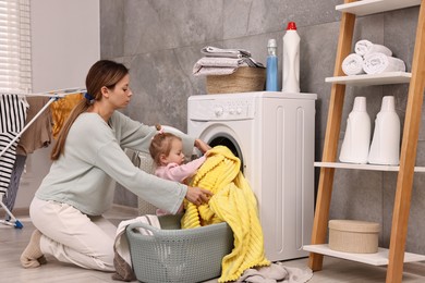 Photo of Housewife with her little daughter doing laundry at home