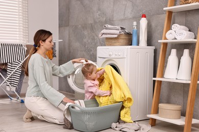 Photo of Housewife with her little daughter doing laundry at home