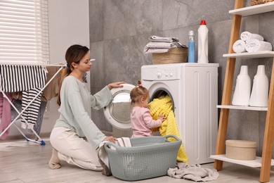 Photo of Housewife with her little daughter doing laundry at home