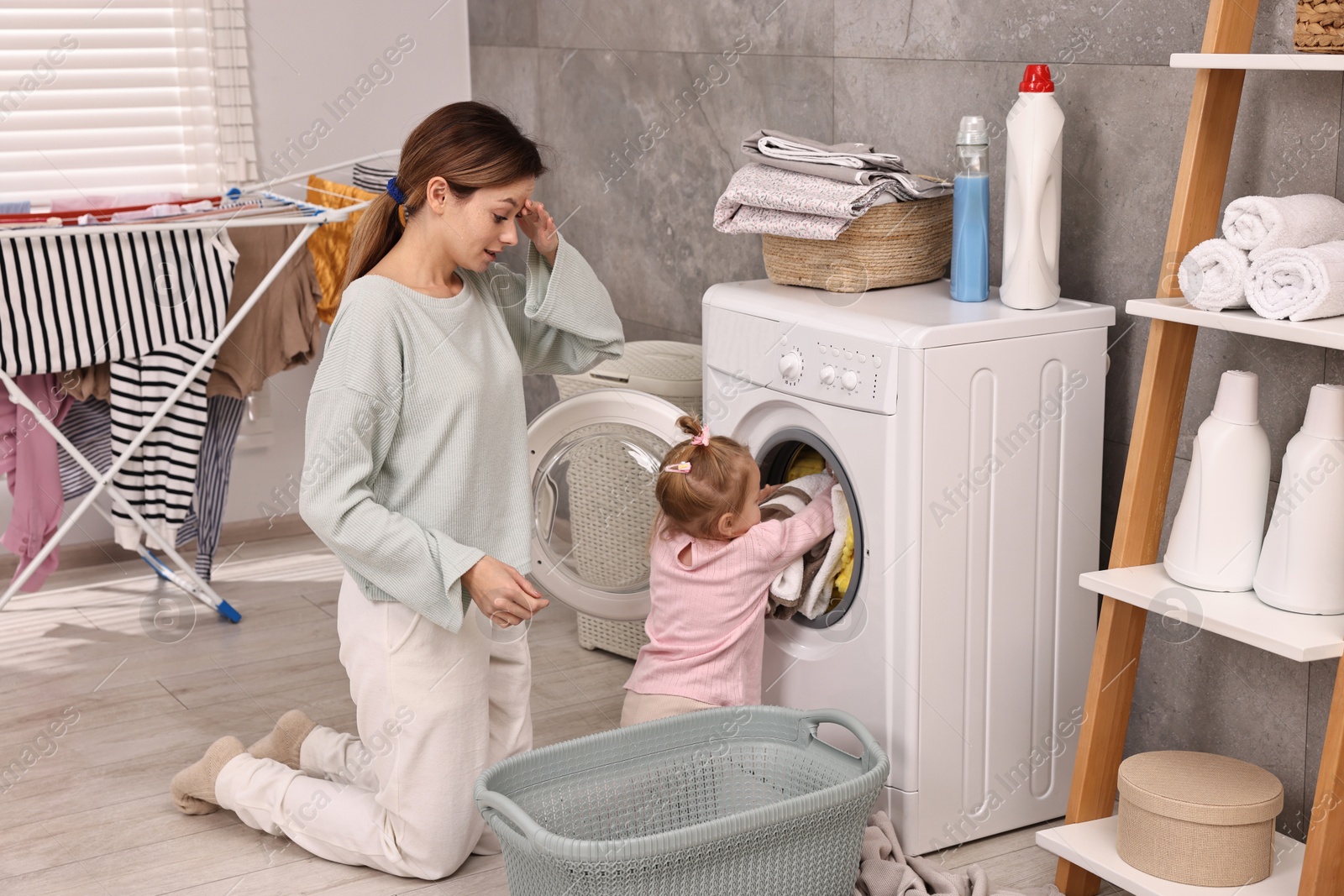 Photo of Housewife with her little daughter doing laundry at home