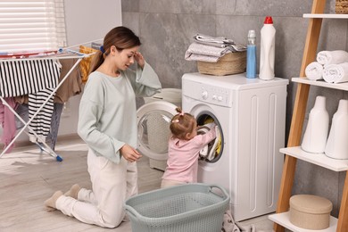 Photo of Housewife with her little daughter doing laundry at home