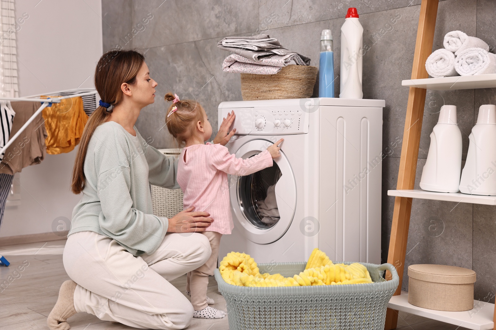 Photo of Housewife with her little daughter doing laundry at home